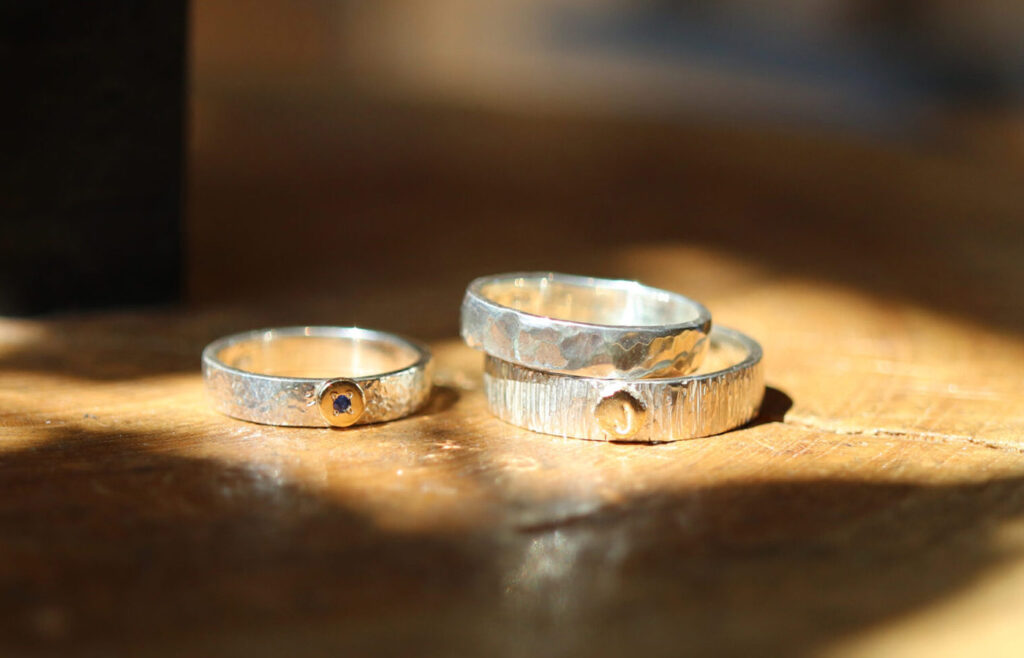 Three handmade sterling silver rings with textured finishes and 18K gold accents